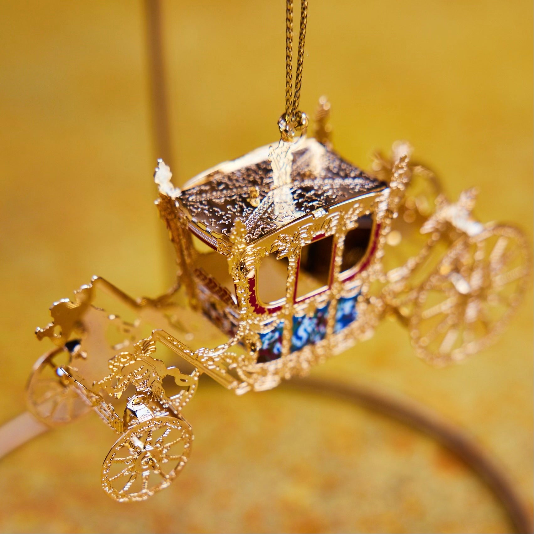 Handcrafted Gold State Coach Christmas Tree Ornament, featuring intricate 24-carat gold details. A stunning royal carriage replica by The London Christmas Company, perfect for adding British elegance to your festive decor. Seen here hanging on a hook.